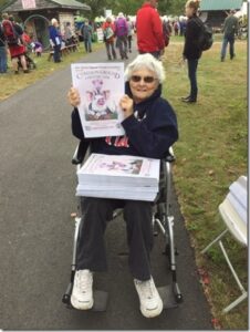 Older woman in wheelchair holding stack of newspapers with a pig on the cover