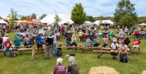 People sit at picnic tables and on hay bales at the Common Ground Country Fair