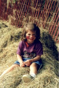 Child with ladybugs painted on her cheeks sitting in a haystack
