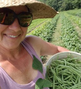 Farmer smiling in straw hat and sunglasses holding a bucket of green beans