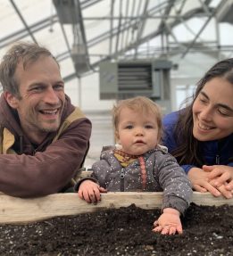 Two smiling farmers look on as a baby plays with potting soil