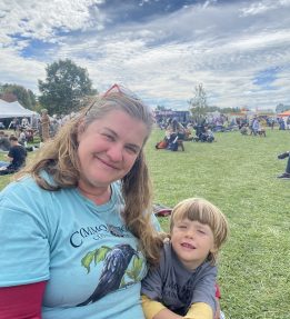 MOFGA Volunteer Jenny Jacques sits with a child on the common at the Common Ground Country Fair.