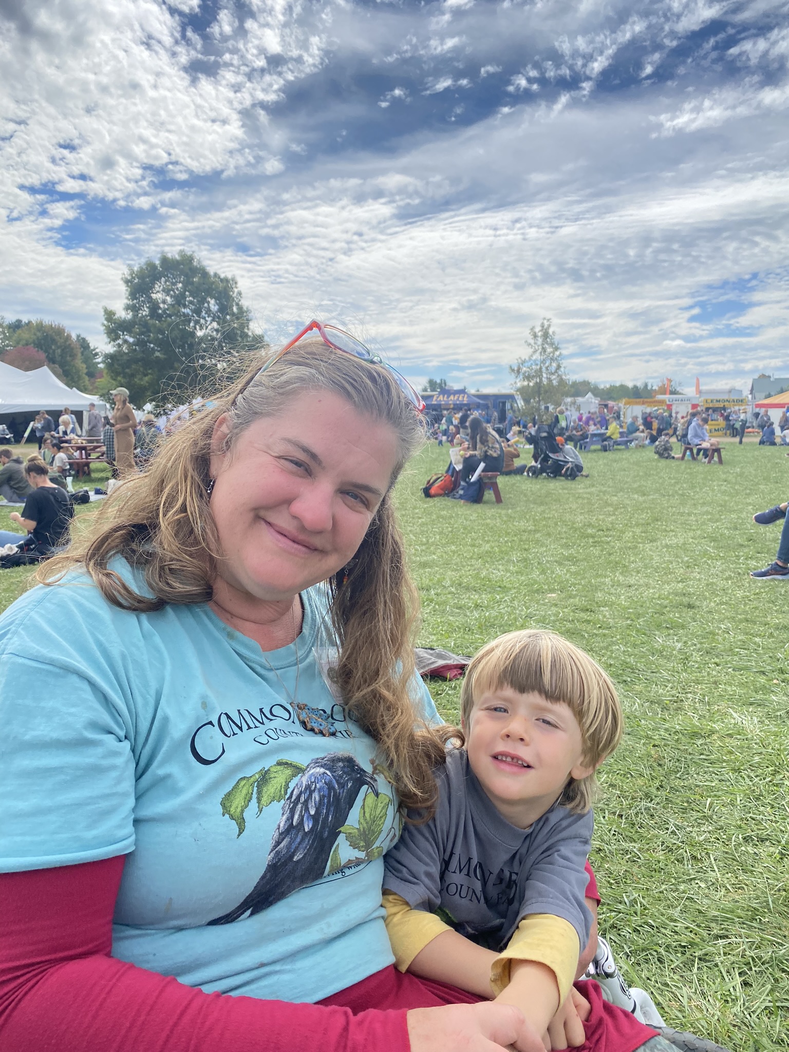 MOFGA Volunteer Jenny Jacques sits with a child on the common at the Common Ground Country Fair.