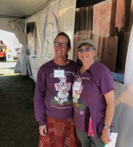 Two Common Ground Country Fair volunteers wear matching purple shirts with pig illustrations